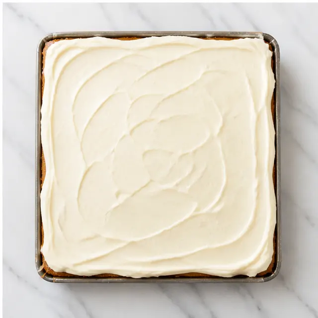 Step 4: Spreading the white cream cheese frosting over the chilled bars