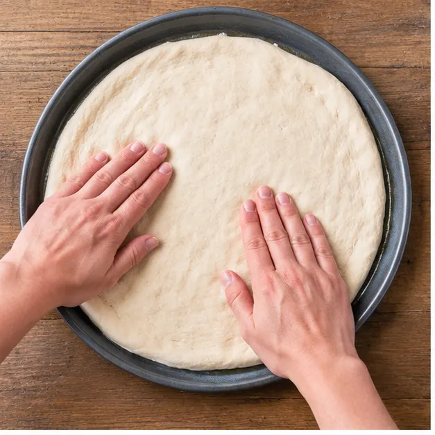 Step 1: pressing and stretching raw pizza dough flat across a round pizza pan